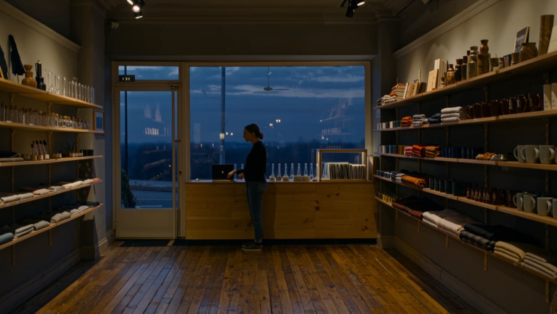 A shopkeeper closing up for the evening, laptop open on the counter